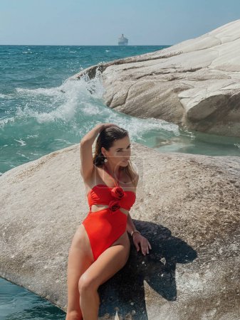 Téléchargez les photos : Photo de mode en plein air de belle femme aux cheveux foncés dans un élégant maillot de bain posant sur la plage rocheuse - en image libre de droit