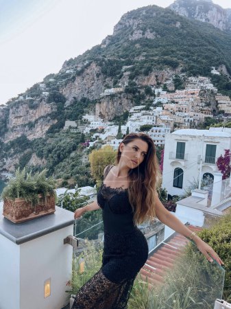 Foto de Foto de viaje de moda de mujer hermosa con el pelo oscuro en ropa elegante posando sobre el telón de fondo de la ciudad Positano en Italia - Imagen libre de derechos