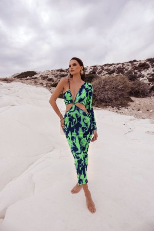 Foto de Foto de moda al aire libre de la hermosa mujer con el pelo oscuro en ropa elegante y accesorios posando sobre rocas blancas cerca del mar en Chipre - Imagen libre de derechos