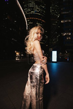 Photo for Fashion outdoor photo of beautiful woman with blond hair in elegant dress and accessories walks around the night city with skyscrapers in the background - Royalty Free Image