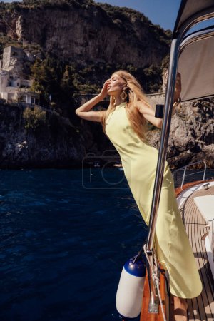 Photo for Fashion travel photo of beautiful sexy woman with blond hair in elegant dress relaxing on the yacht in Italy, Positano city on background - Royalty Free Image