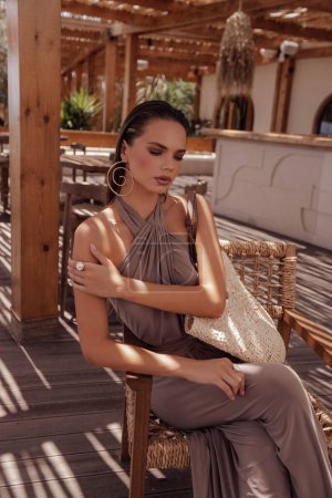 Téléchargez les photos : Mode photo en plein air de belle femme aux cheveux foncés dans des vêtements élégants avec des accessoires posant dans le club de plage d'été à Chypre - en image libre de droit