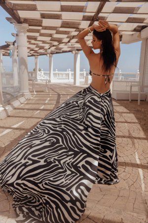 Foto de Foto de moda al aire libre de la hermosa mujer con el pelo oscuro en vestido elegante con estampado de cebra posando en el club de playa - Imagen libre de derechos