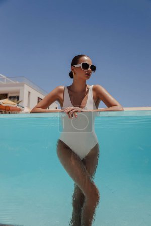 Photo for Fashion outdoor photo of beautiful woman with dark hair in elegant swimming suit and accessories relaxing in swimming pool in summer beach club - Royalty Free Image
