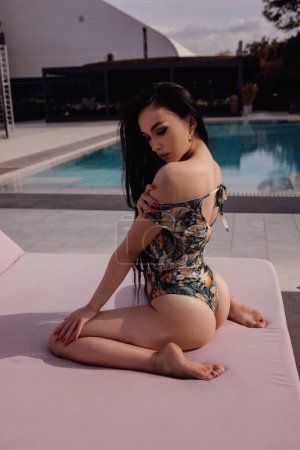 Photo for Fashion outdoor photo of beautiful woman with dark hair in elegant swimming suit relaxing near swimming pool in beach club - Royalty Free Image