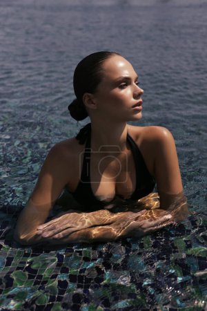 Foto de Foto de moda al aire libre de la hermosa mujer con el pelo oscuro en traje de baño elegante relajante en la piscina en el club de playa al aire libre en Chipre - Imagen libre de derechos