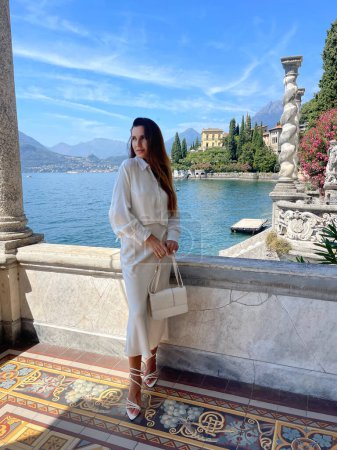 Téléchargez les photos : Photo de mode en plein air de belle femme aux cheveux foncés dans des vêtements élégants posant dans une villa luxueuse au lac de Côme en Italie - en image libre de droit