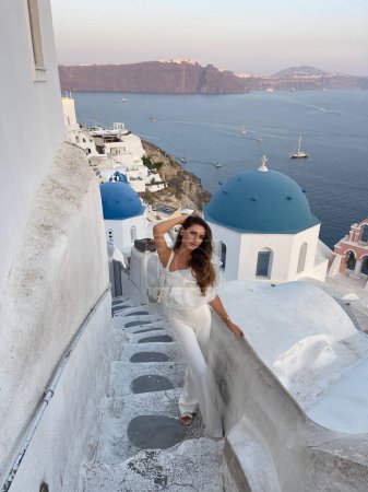Foto de Foto al aire libre de moda de mujer hermosa con cabello oscuro en ropa elegante con accesorio que viaja por la isla de Santorini - Imagen libre de derechos