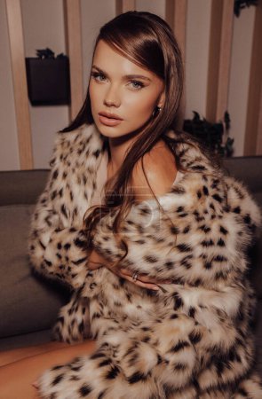 Téléchargez les photos : Photo de mode de belle femme aux cheveux foncés en manteau de fourrure de lynx luxueux posant dans un intérieur élégant - en image libre de droit