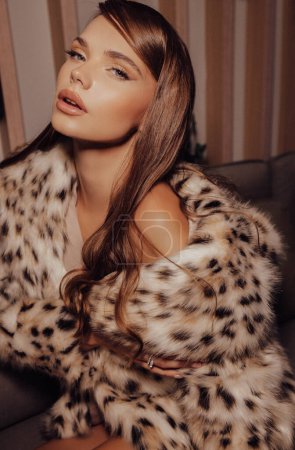 Téléchargez les photos : Photo de mode de belle femme aux cheveux foncés en manteau de fourrure de lynx luxueux posant dans un intérieur élégant - en image libre de droit