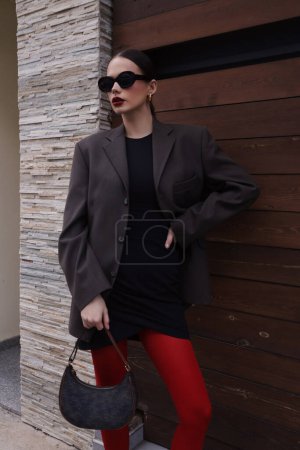 Téléchargez les photos : Photo de mode en plein air de belle femme brune en tenue élégante, collants rouges et veste - en image libre de droit