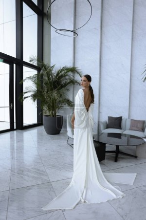 Foto de Foto de moda de la novia hermosa en vestido de novia elegante y accesorios posando en habitación de hotel elegante - Imagen libre de derechos