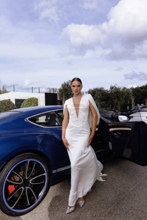 Téléchargez les photos : Photo de mode de belle mariée dans la robe de mariée élégante et accessoires posant près de voiture de luxe - en image libre de droit