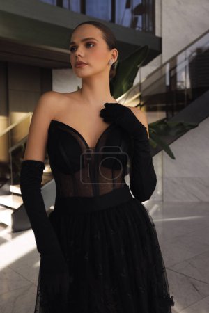 Photo for Fashion photo of beautiful woman with dark hair in elegant black dress with accessories posing in luxurious hotel lobby - Royalty Free Image