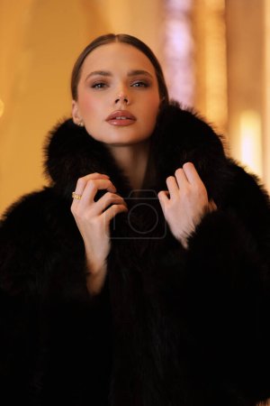 Photo for Fashion interior photo of beautiful sensual woman with dark hair in luxurious black fur coat and jewelry posing in hall of the hotel - Royalty Free Image