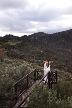 Téléchargez les photos : Mode photo en plein air de belle femme aux cheveux foncés dans une robe de mariée luxueuse avec des bijoux posant dans un bel endroit de la nature Lefkara, avec des montagnes en arrière-plan - en image libre de droit