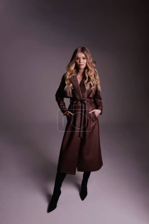 Foto de Foto de moda de una hermosa mujer con cabello rubio en lujoso abrigo marrón de cuero posando en el estudio - Imagen libre de derechos
