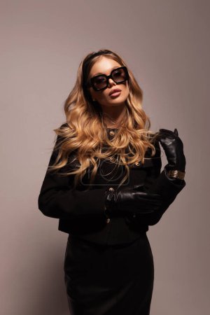 Photo for Fashion photo of beautiful girl with blond hair in eleegant jacket, leather skirt and sunglasses posing in studio - Royalty Free Image