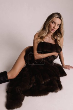 Téléchargez les photos : Photo de mode de belle femme sexy aux cheveux blonds en manteau de fourrure luxueux posant en studio - en image libre de droit