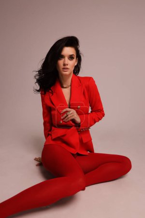 Téléchargez les photos : Photo de mode de belle femme aux cheveux foncés en costume rouge luxueux posant en studio - en image libre de droit