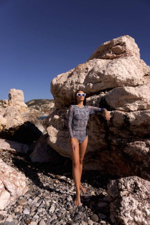 Foto de Foto de moda al aire libre de la hermosa mujer con el pelo oscuro en ropa de playa elegante posando en la playa en Chipre - Imagen libre de derechos
