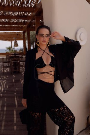 Foto de Foto de moda de una hermosa mujer con cabello oscuro en ropa elegante con accesorios posando en el club de playa de verano - Imagen libre de derechos