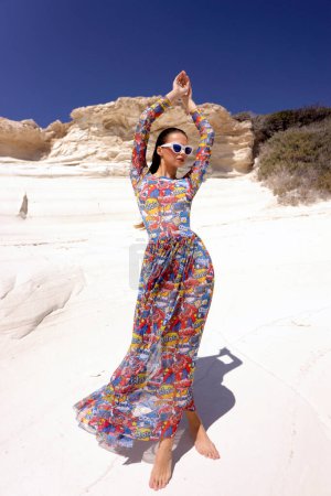 Téléchargez les photos : Photo de mode en plein air de belle femme sensuelle avec les cheveux foncés dans des vêtements de plage imprimés élégants posant dans la plage de roche blanche sur Chypre - en image libre de droit