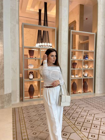 Photo for Fashion photo of beautiful sensual woman with dark hair in luxurious white clothes with accessories posing in elegant lobby hotel - Royalty Free Image