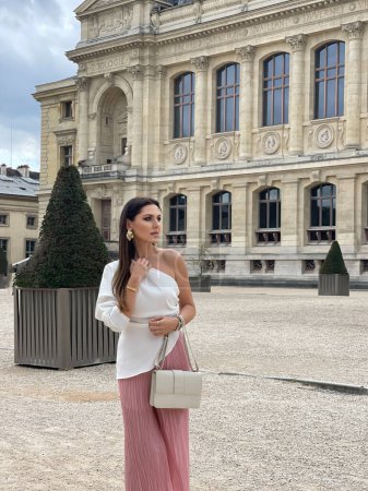 Photo for Fashion outdoor photo of beautiful woman with dark hair in elegant clothes with accessories posing in beautiful Paris garden with beautiful monument - Royalty Free Image