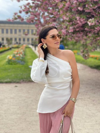 Photo for Fashion outdoor photo of beautiful woman with dark hair in elegant clothes with accessories posing in spring garden with blossom sakura tree - Royalty Free Image