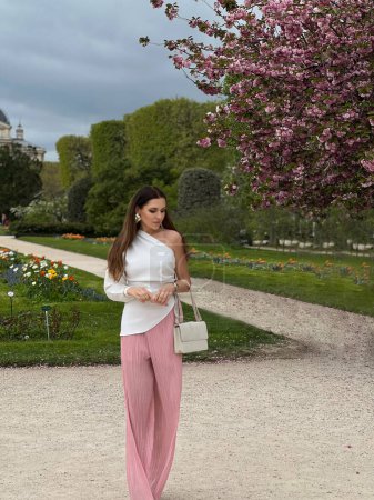 Photo for Fashion outdoor photo of beautiful woman with dark hair in elegant clothes with accessories posing in spring garden with blossom sakura tree - Royalty Free Image