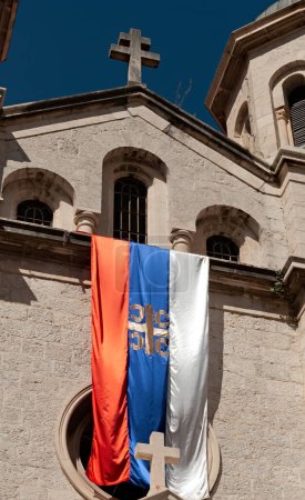 Téléchargez les photos : Le drapeau de l'église orthodoxe serbe étant sur la façade du temple orthodoxe serbe Saint-Nicolas sur la vieille ville de Kotor au Monténégro - en image libre de droit