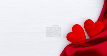 Red hearts and red satin on the white wooden background. Red ribbon. Valentine's Day gift.