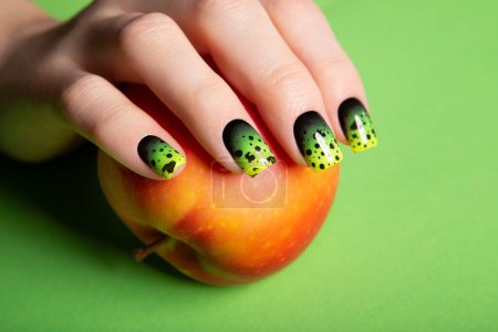 Téléchargez les photos : Female neat hand with short natural nails painted with green nail polish holding apple. Natural, cozy, elegant, modern look. High-quality photo - en image libre de droit