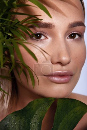 Photo for Young beautiful woman with green leave near face and body. Skin care beauty treatments concept. Closeup girls face with green leave. White model with clean, health skin of face - posing at studio - Royalty Free Image
