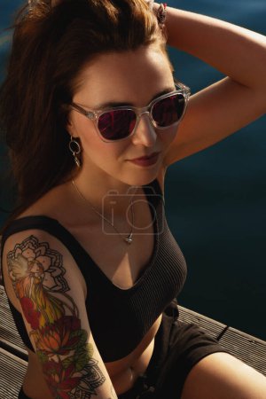 Foto de Foto de moda de una hermosa mujer bronceada con cabello castaño en traje deportivo relajándose junto a una piscina. Foto de alta calidad - Imagen libre de derechos