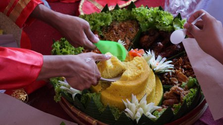 Foto de Chef que sirve nasi tumpeng (arroz con cono) servido con urap-urap (ensalada indonesia), pollo frito y fideos. Nasi tumpeng se sirve generalmente en fiestas de cumpleaños o Acción de Gracias - Imagen libre de derechos