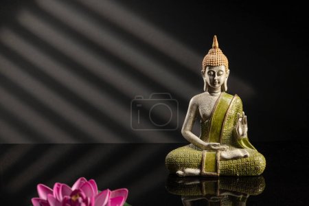 Buddha statue in meditation with shadows on dark background with copy space.