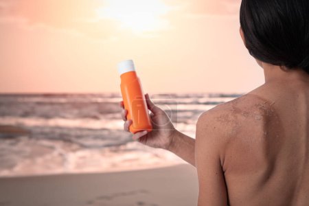 Téléchargez les photos : Dos de femme avec des coups de soleil tenant bouteille de crème solaire. Isolé sur fond blanc avec espace de copie. Format vertical - en image libre de droit