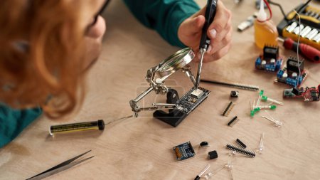 Téléchargez les photos : Cropped male technician or engineer soldering microcircuit with soldering iron under magnifying glass at table with variety technical tools and components. Modern technology and innovation - en image libre de droit