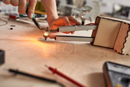 Photo for Selective focus of partial male technician or engineer doing experiment with technical equipment and forceps at wooden table. Modern science, technology and innovation - Royalty Free Image