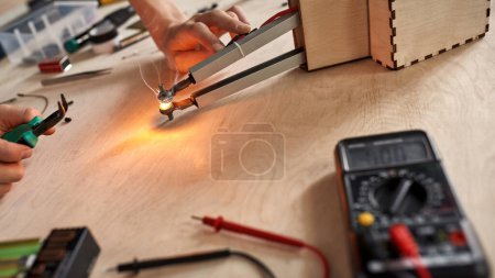 Photo for Selective focus of cropped male technician or engineer doing experiment with technical equipment and forceps at wooden table. Modern science, technology and innovation - Royalty Free Image