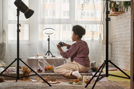 Distanzaufnahme einer schwarzen Fotografin, die Muscheln auf einer Digitalkamera im heimischen Studio fotografiert. Junge Mädchen erstellen Inhalte für Fotoaktien, Handel, soziale Netzwerke und Werbung. Fernbedienung