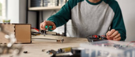 Photo for Cropped male technician or engineer doing technical experiment with equipment, forceps and voltmeter at blurred wooden table. Modern science, technology and innovation - Royalty Free Image