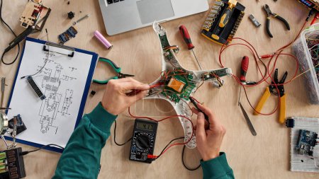 Photo for Top view of cropped male IT technician or engineer checking broken drone with voltmeter on table with variety technical tools and components. Modern technology and innovation - Royalty Free Image