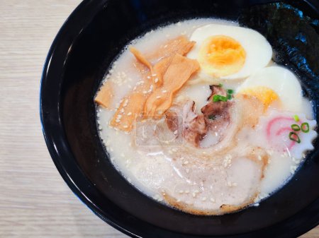 Photo for Tonkotsu ramen in a black cup topped with chashu pork, Naruto fish balls, soy-sauce pickled eggs, menma bamboo shoots and seaweed. Ramen is a distinctive Japanese style noodle soup. - Royalty Free Image