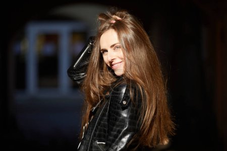 Téléchargez les photos : Jeune belle fille aux cheveux longs en veste en cuir noir regardant la caméra - en image libre de droit