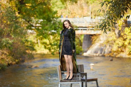 Téléchargez les photos : Belle jeune femme debout sur une chaise près de la rivière - en image libre de droit