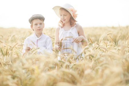 Photo for Portrait of happy boy and girl in hats standing in wheat field - Royalty Free Image