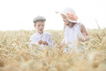 Foto de Retrato de niño y niña felices en sombreros de pie en el campo de trigo - Imagen libre de derechos
